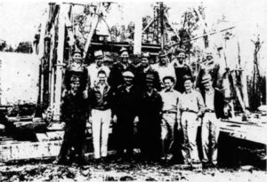 Drilling crew members stand in front of their 1938 giant oilfield discovery well at Magnolia, Arkansas. 