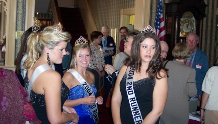 Three of the young women with sashes and tiaras smiling at a reception.