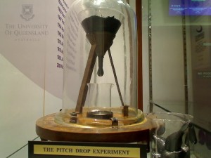 Pitch drop experiment photo of a glass globe with a funnel bottom and a drip years in the making.