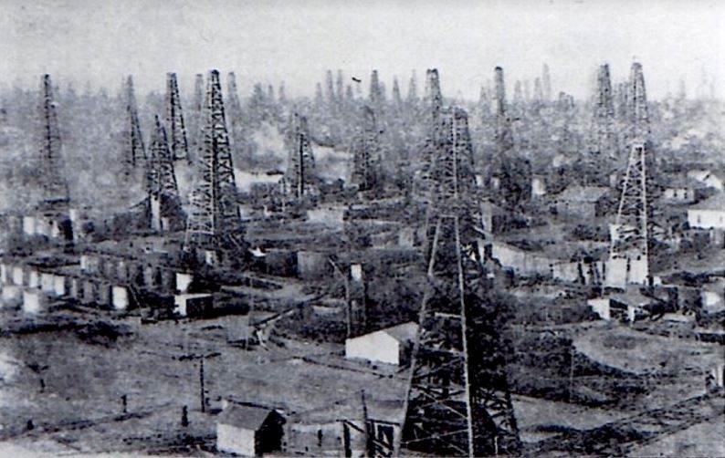 Common scene of early oil booms: drilling derricks, tanks and engine houses the the horizon.