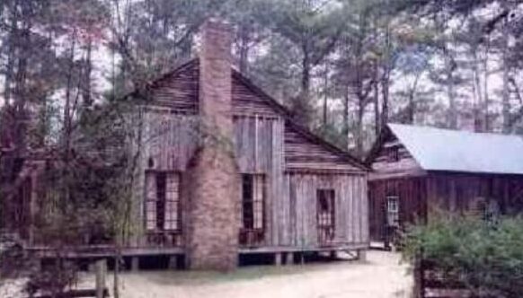 Exterior color image of the Barret homestead cabin and brick fireplace.