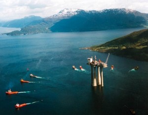 The "Troll A" natural gas platform operated by Statoil is towed from its Norwegian port by eight tugs with mountains in background.